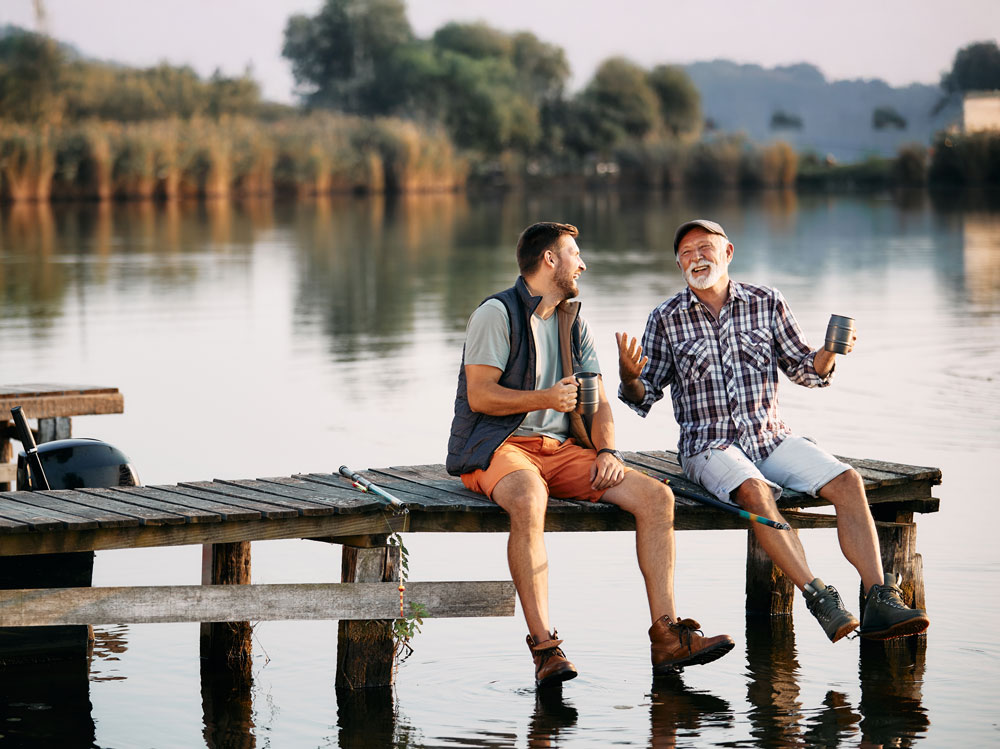 Caucasian father and adult son relaxing on a dock by the water.