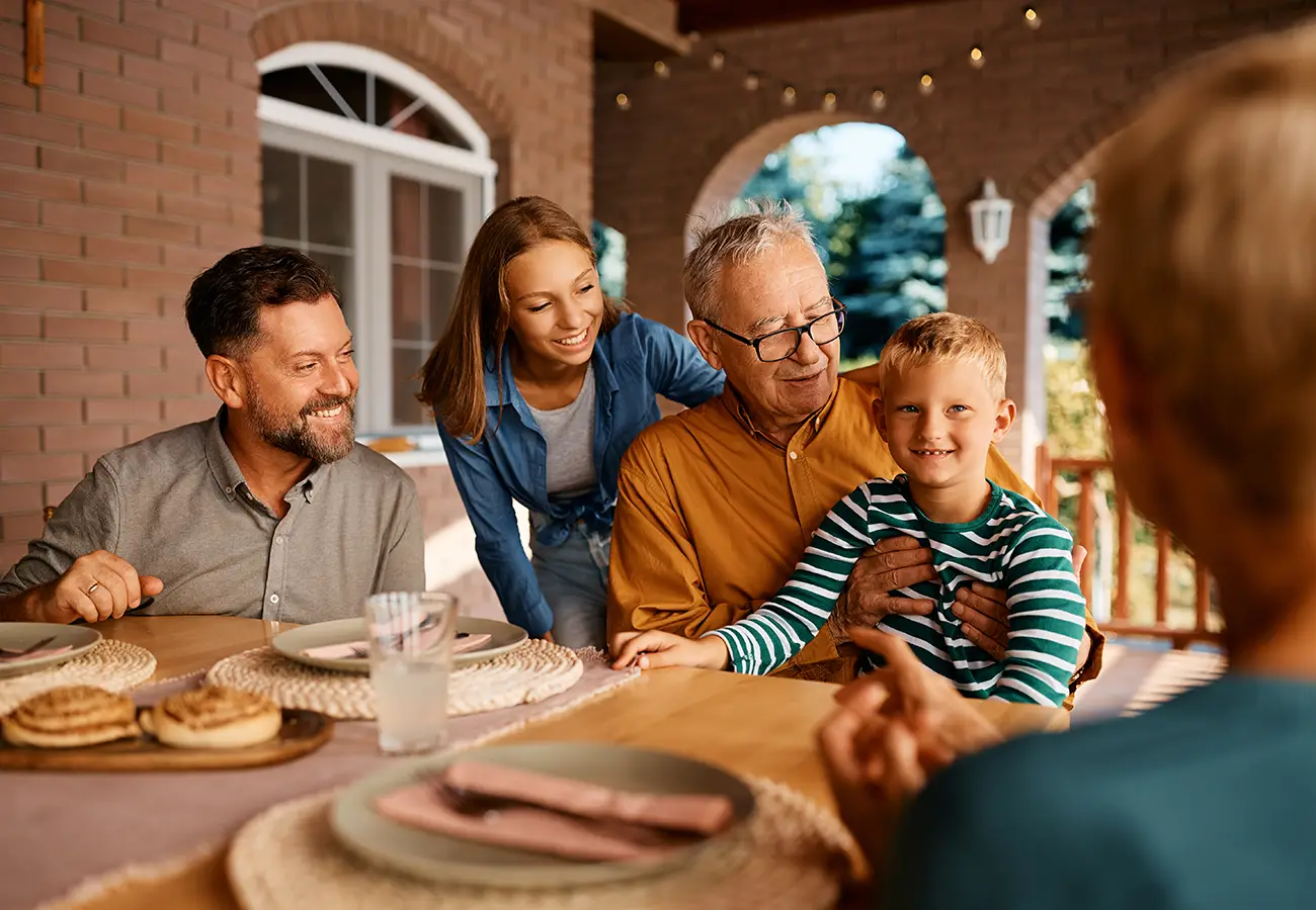 Family gathered at a dinner table with a young blonde boy sitting on his grandfather’s lap.